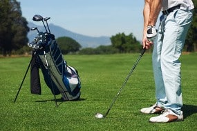 golfer man hitting golf ball from green fairway alone with bag on stand